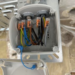 ProfiMajster usługi elektryczne - Otwarta puszka elektryczna z widocznymi, kolorowymi przewodami połączonymi szybkozłączkami Wago, zamocowana na perforowanej korytku kablowym.