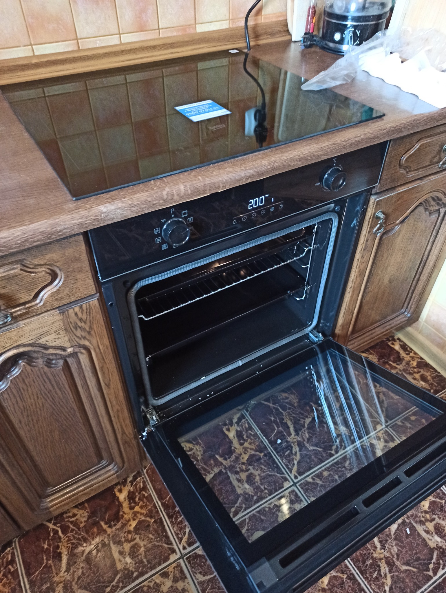 Podłączenie piekarnika elektrycznego w zabudowie kuchennej w Bydgoszczy. Widoczna płyta indukcyjna i otwarte drzwiczki piekarnika. Drewniane szafki.