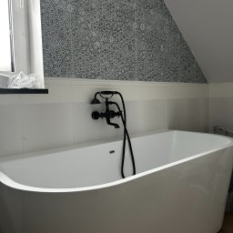 Usługi remontowo-budowlane Ireneusz Frontczak - Nowoczesna, biała wanna wolnostojąca z czarną armaturą na tle ściany z geometrycznym wzorem w wykończonej łazience na poddaszu. Minimalistyczny design.