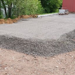 Piotr Wasiluk - Przygotowany teren pod kostkę brukową z użyciem kruszywa, widoczny fragment koparki i wytyczone granice. Etap prac przed ułożeniem kostki.