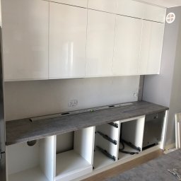 Mikołaj Nowak - Białe, lakierowane szafki kuchenne w trakcie montażu. Widoczny poziomica, szuflady bez frontów i narzędzia. Nowoczesna kuchnia w jasnych barwach.
