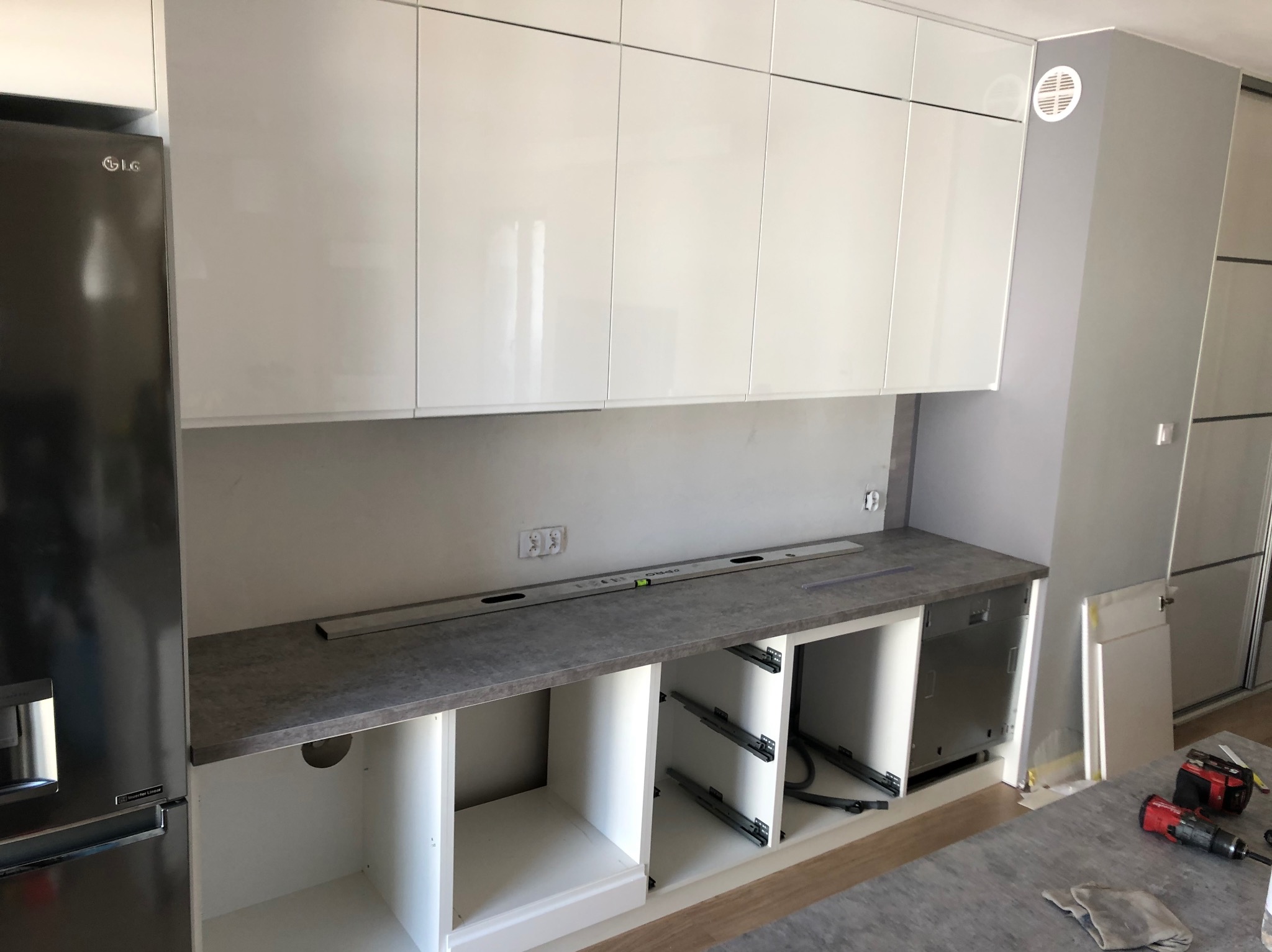 Białe, lakierowane szafki kuchenne w trakcie montażu. Widoczny poziomica, szuflady bez frontów i narzędzia. Nowoczesna kuchnia w jasnych barwach.