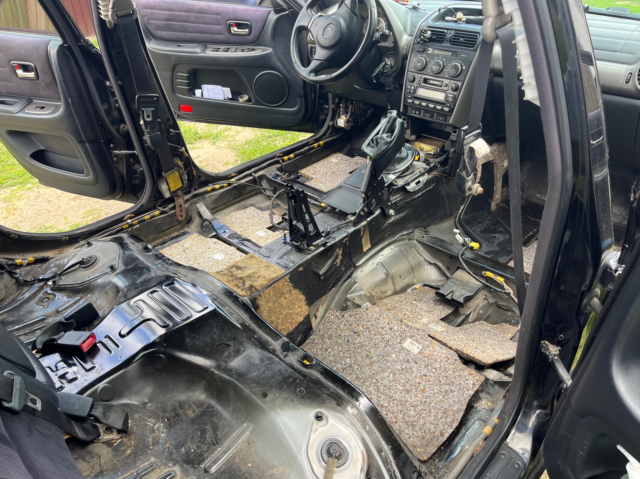 Wnętrze samochodu w trakcie demontażu, widoczne częściowo zdjęte obicia podłogowe, elementy deski rozdzielczej i siedzenia. Prace demontażowe w pojeździe.