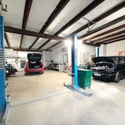 Evo Tune Oborniki Śląskie - Wnętrze warsztatu samochodowego z dwoma podnośnikami, czerwonym autem z otwartym bagażnikiem i czarnym autem z podniesioną maską. Widoczne narzędzia i wyposażenie warsztatowe.