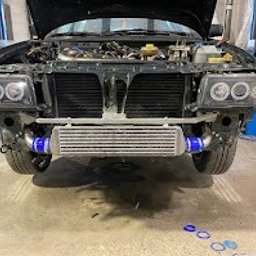 Evo Tune Oborniki Śląskie - Czarny samochód z otwartą maską i zamontowanym intercoolerem, widoczne nowe reflektory z ringami. Warsztatowy podnośnik w tle, ślady opon na posadzce.