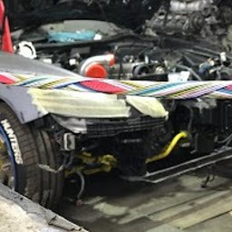 Evo Tune Oborniki Śląskie - Przód szarego auta w warsztacie, z widocznym turbodoładowaniem i elementami tuningowymi. Taśma zabezpieczająca na karoserii, niebieskie felgi. Silnik w tle.