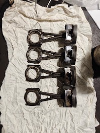 Cztery tłoki silnika spalinowego ułożone na szmatce w warsztacie w Obornikach Śląskich. Widoczne ślady użytkowania i nagar na elementach.