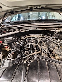 Otwarta maska samochodu z widocznym silnikiem w trakcie naprawy. Detale mechaniczne, przewody i elementy silnika w zbliżeniu. Oświetlenie warsztatowe.