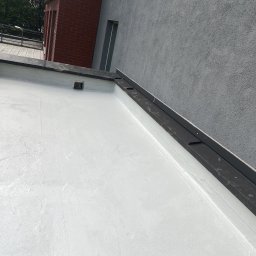 R-dach Robert Szelwach - Biała, płaska powierzchnia dachu po renowacji, z widocznymi obróbkami blacharskimi i fragmentem ściany budynku w tle. Ujęcie z góry.