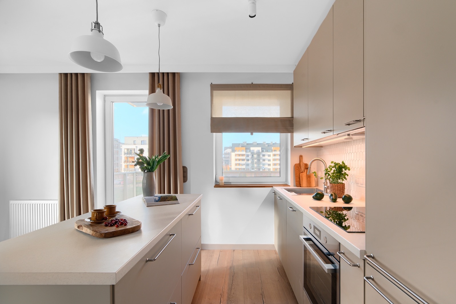 Jasna kuchnia w neutralnych barwach z drewnianymi akcentami. Widok na miasto przez okno. Minimalistyczny design, oświetlenie punktowe i wiszące lampy.