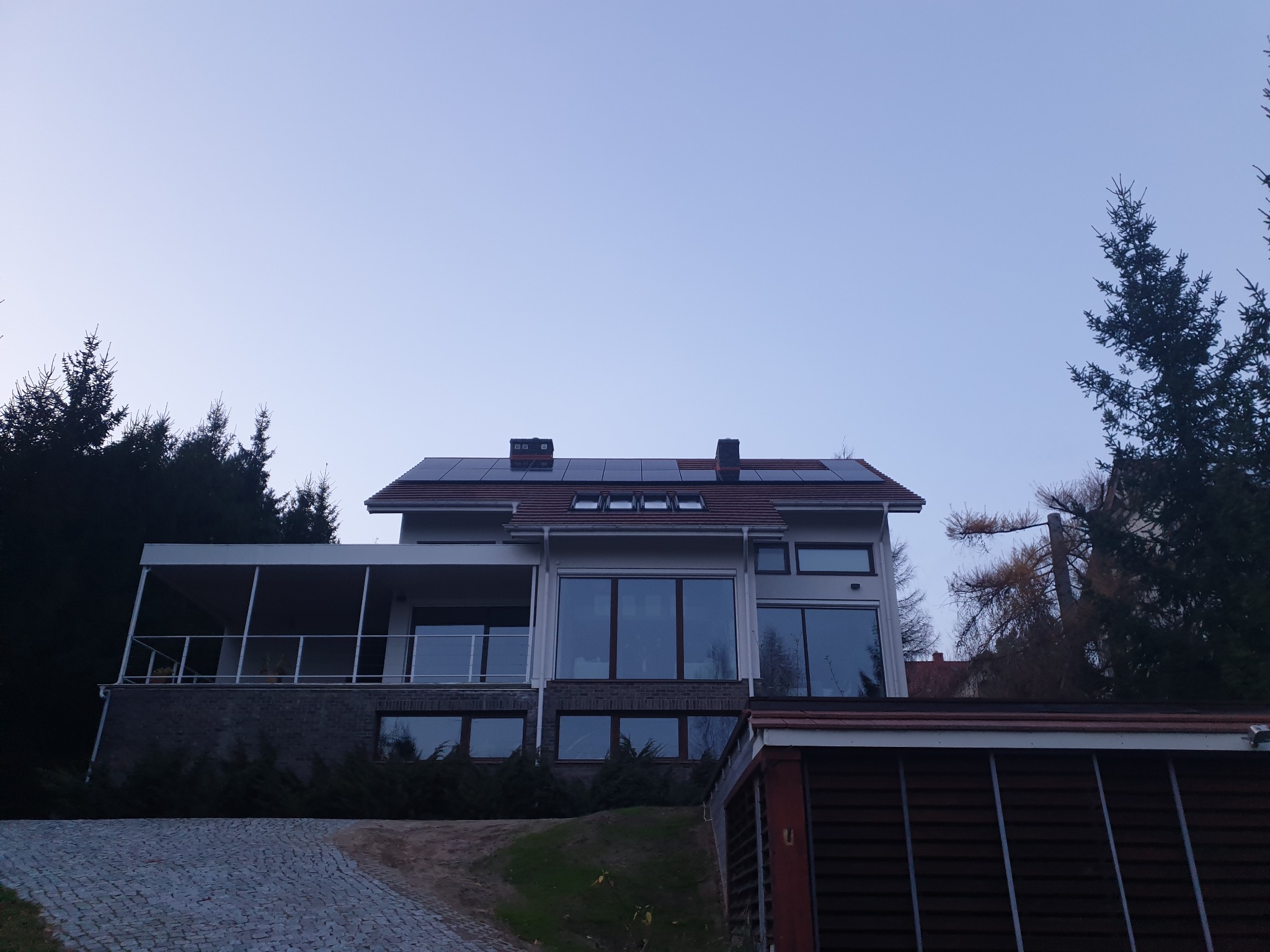 Dom jednorodzinny z panelami słonecznymi na dachu, widok z dołu, błękitne niebo w tle. Instalacja 10 kwp.