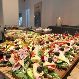 SOSNOWIECKA SIEĆ SZEROKOPASMOWA SPÓŁKA Z OGRANICZONĄ ODPOWIEDZIALNOŚCIĄ - Bogato zdobione kanapki na drewnianej desce, idealne na event w Sosnowcu. Różnorodność składników: szynka, ser, warzywa, oliwki. Elegancki catering.