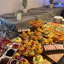 SOSNOWIECKA SIEĆ SZEROKOPASMOWA SPÓŁKA Z OGRANICZONĄ ODPOWIEDZIALNOŚCIĄ - Bogato zastawiony stół z różnorodnymi przekąskami: mini burgery, wędliny, sery, sałatki i desery. Dekoracje świąteczne w tle. Idealne na elegancki catering.