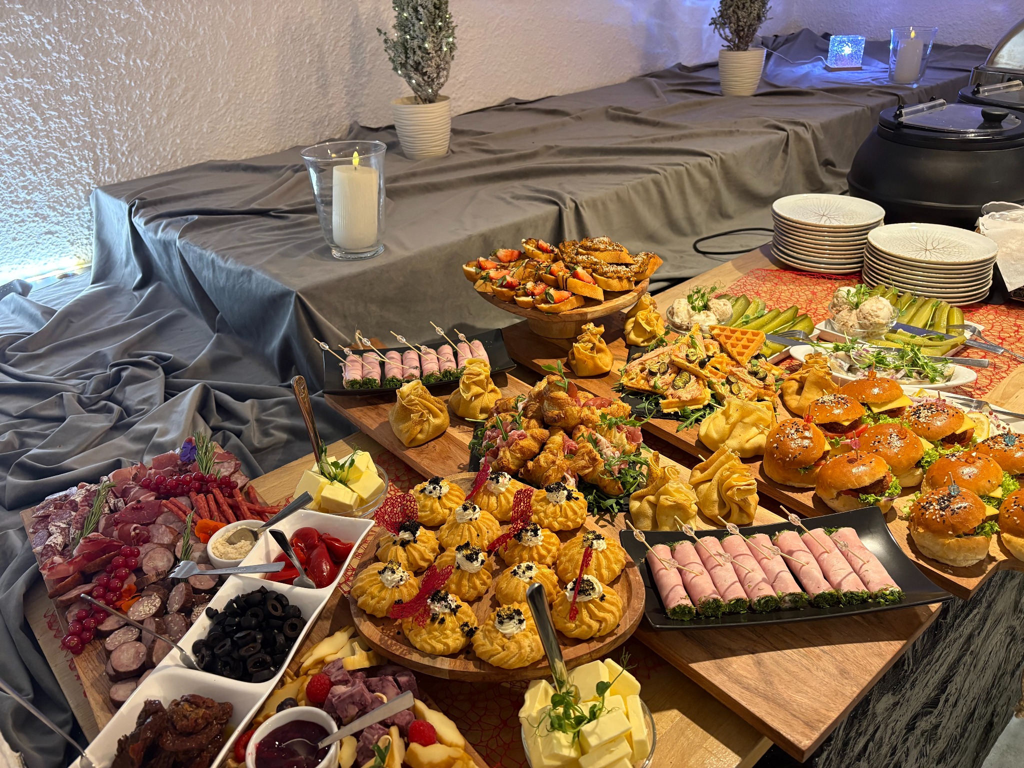 Bogato zastawiony stół z różnorodnymi przekąskami: mini burgery, wędliny, sery, sałatki i desery. Dekoracje świąteczne w tle. Idealne na elegancki catering.