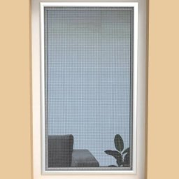 PergoleTarasy.pl - Zamontowana moskitiera w oknie z białymi ramami, widok na wnętrze z szarą sofą i rośliną. Delikatna siatka moskitiery zapewnia ochronę przed owadami.