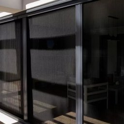 PergoleTarasy.pl - Zasłonięte, przesuwne plisy okienne w kolorze grafitowym, zamontowane na tarasie w Katowicach. Widoczne refleksy światła na powierzchni plis.