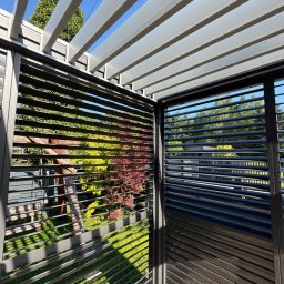Centrum Pergoli i Tarasów - Nowoczesna pergola metalowa z regulowanymi lamelami, widok z dołu na konstrukcję i otaczającą zieleń. Minimalistyczny design, gra światła i cienia.