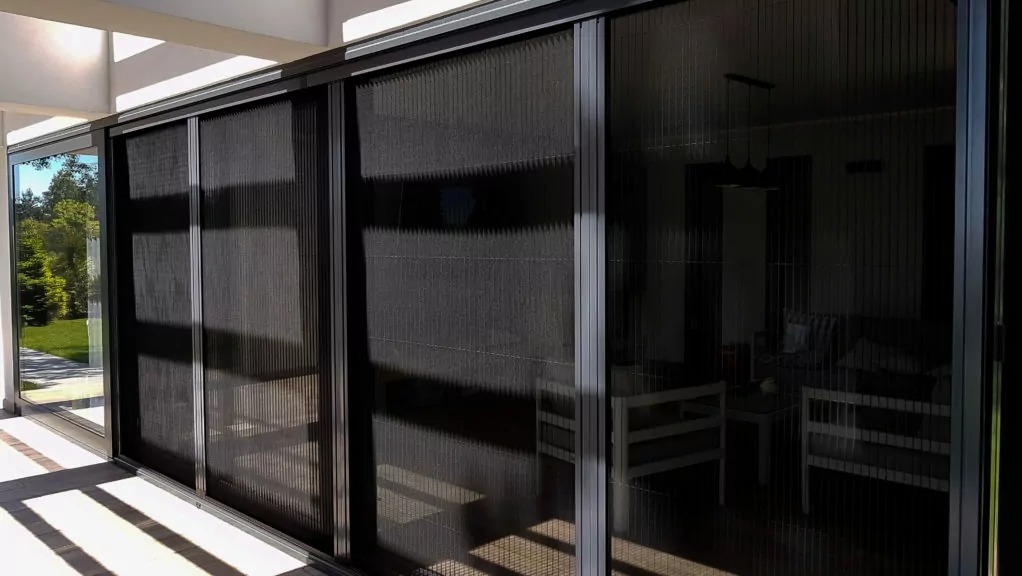 Zasłonięte, przesuwne plisy okienne w kolorze grafitowym, zamontowane na tarasie w Katowicach. Widoczne refleksy światła na powierzchni plis.