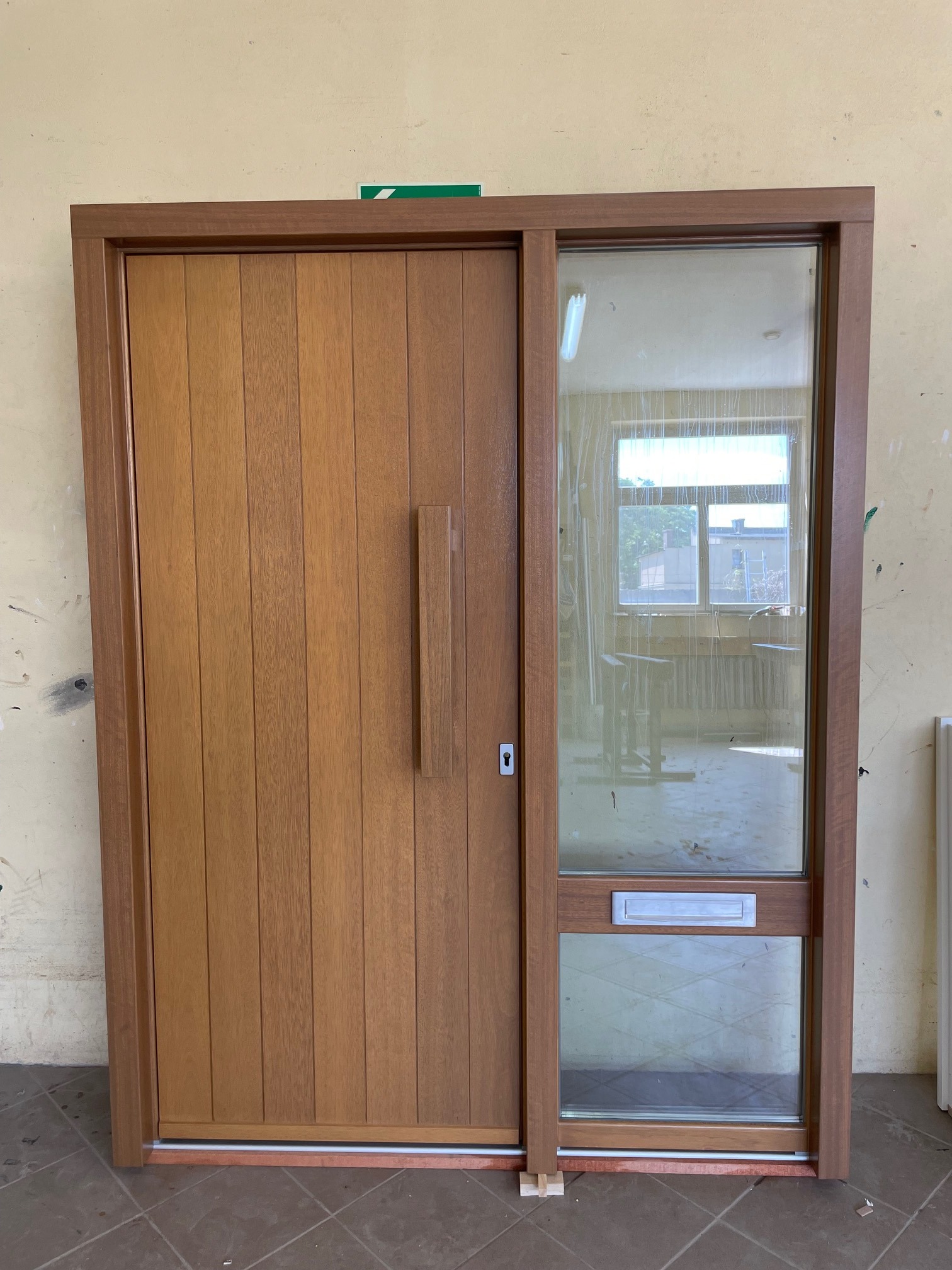 Brązowe drzwi wejściowe z szybą i skrzynką na listy, pionowe panele, widok z przodu, oświetlenie dzienne, minimalistyczny design.