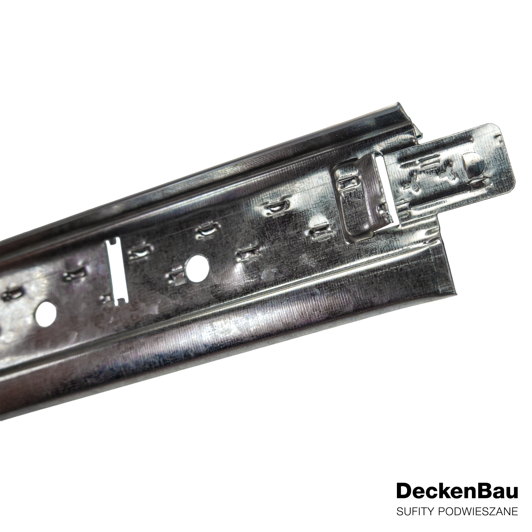 Metalowy profil do montażu sufitów podwieszanych, widoczny z bliska, z logo firmy DeckenBau w prawym dolnym rogu. Element konstrukcyjny z otworami i zaczepami.
