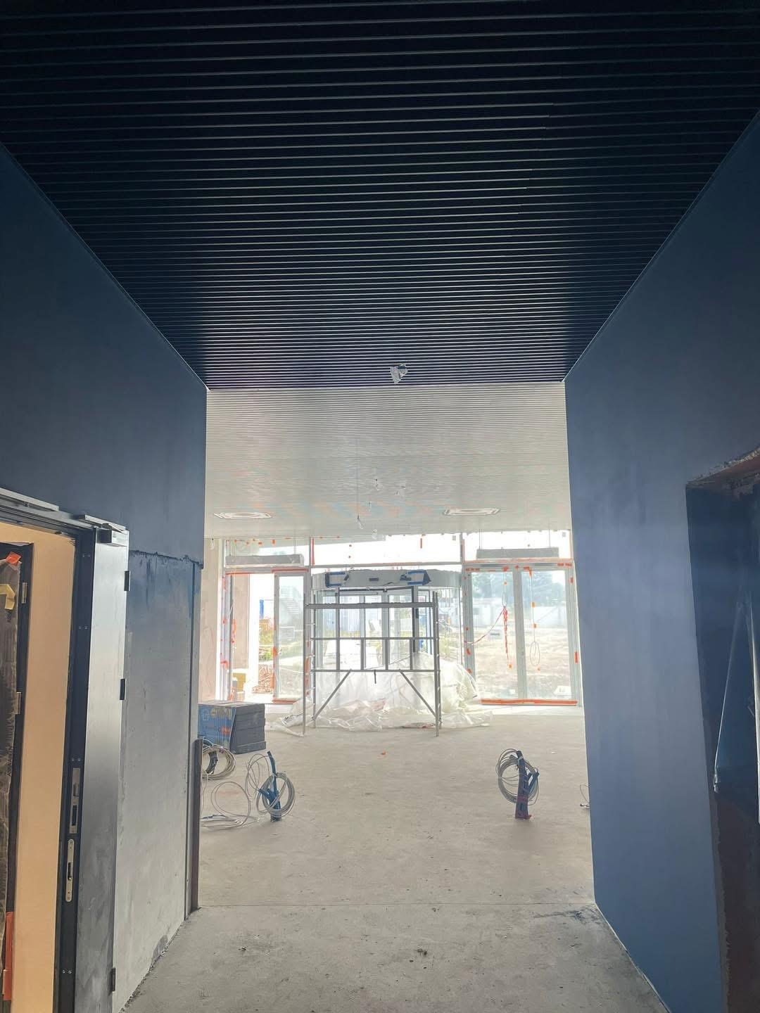 Montaż sufitu rastrowego w biurze w Warszawie. Widok z korytarza na przestrzeń z rusztowaniem i narzędziami. Ściany pomalowane na ciemny kolor.