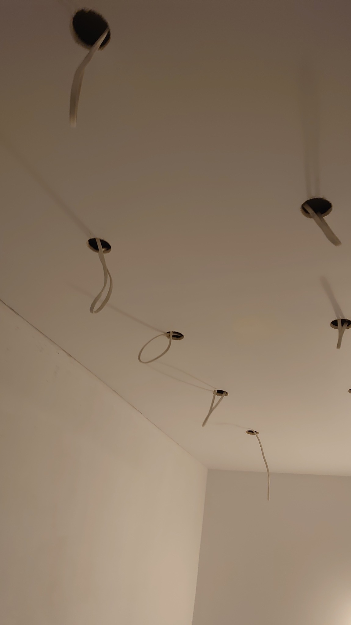 Biały sufit z widocznymi otworami i wystającymi przewodami elektrycznymi, przygotowany do montażu oświetlenia. Widok z dołu, surowy stan wykończenia wnętrza.