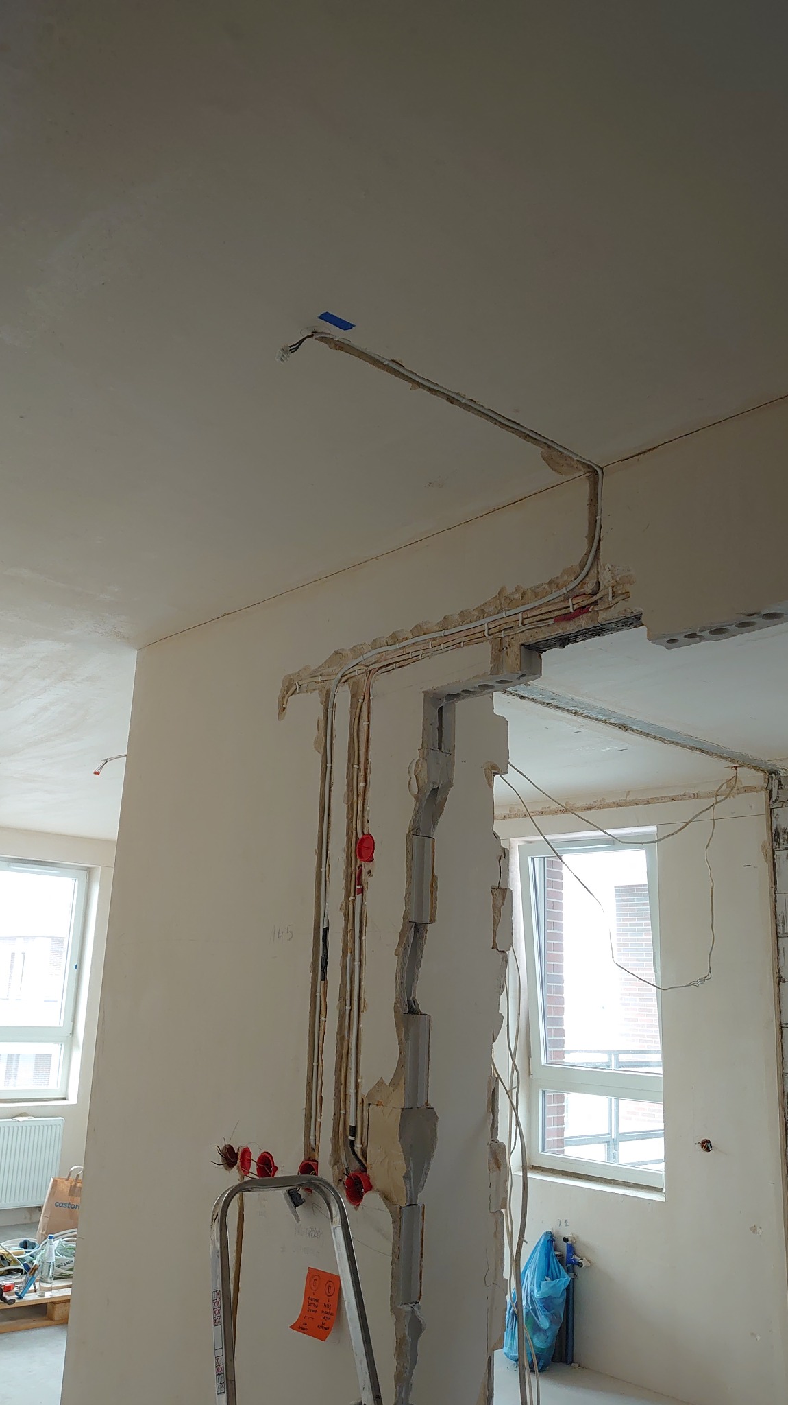 Wnętrze w trakcie remontu: widoczne kable elektryczne prowadzone w ścianach i pod sufitem, puszki elektryczne, drabina i okno. Instalacja elektryczna w trakcie prac.
