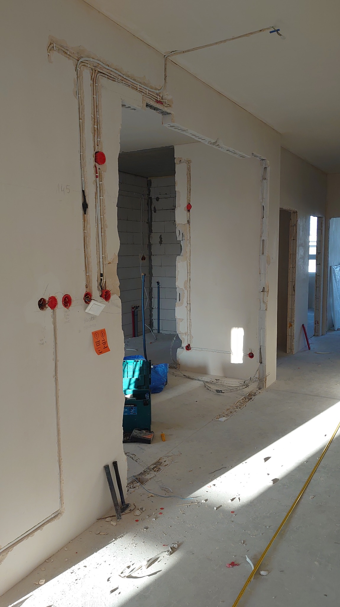 Wnętrze w trakcie remontu: widoczne kable elektryczne w ścianach, puszki instalacyjne i narzędzia. Surowy stan wykończenia, przygotowanie do dalszych prac.