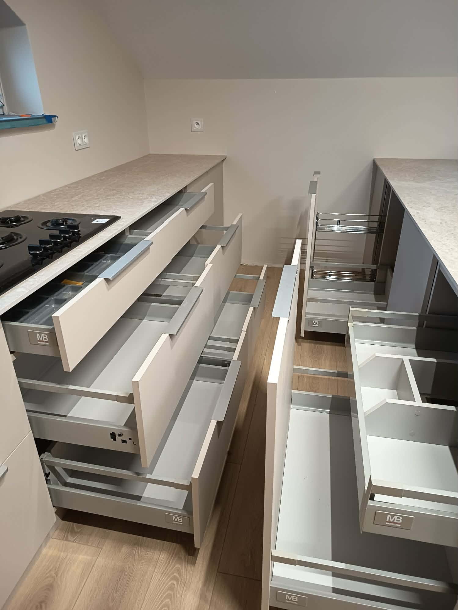 Jasna kuchnia z otwartymi szufladami i systemami cargo, widoczne detale wykończenia i funkcjonalne rozwiązania przechowywania. Uwagę zwraca nowoczesny design.