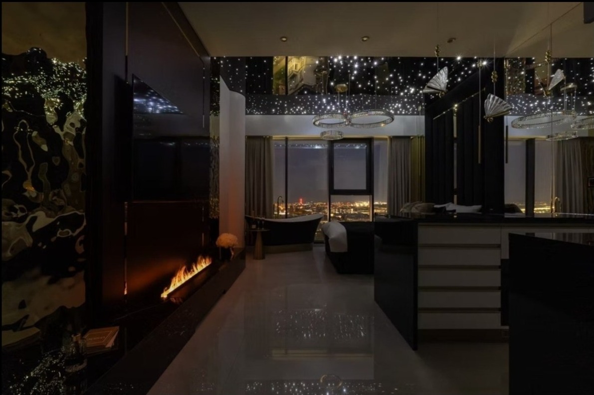 Luksusowy apartament z widokiem na miasto nocą. Czarna wanna wolnostojąca, kominek i sufit z efektem gwiazd tworzą unikalny klimat. Nowoczesne oświetlenie.