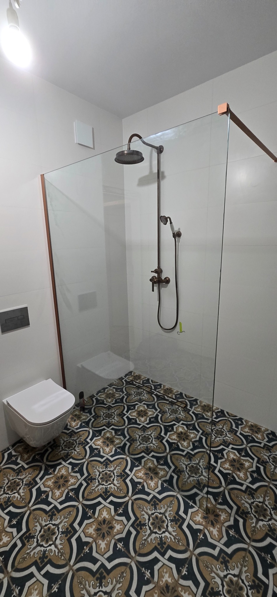 Nowoczesna łazienka z kabiną prysznicową typu walk-in, armaturą w stylu retro i dekoracyjną podłogą w geometryczne wzory. Minimalistyczna toaleta podwieszana.