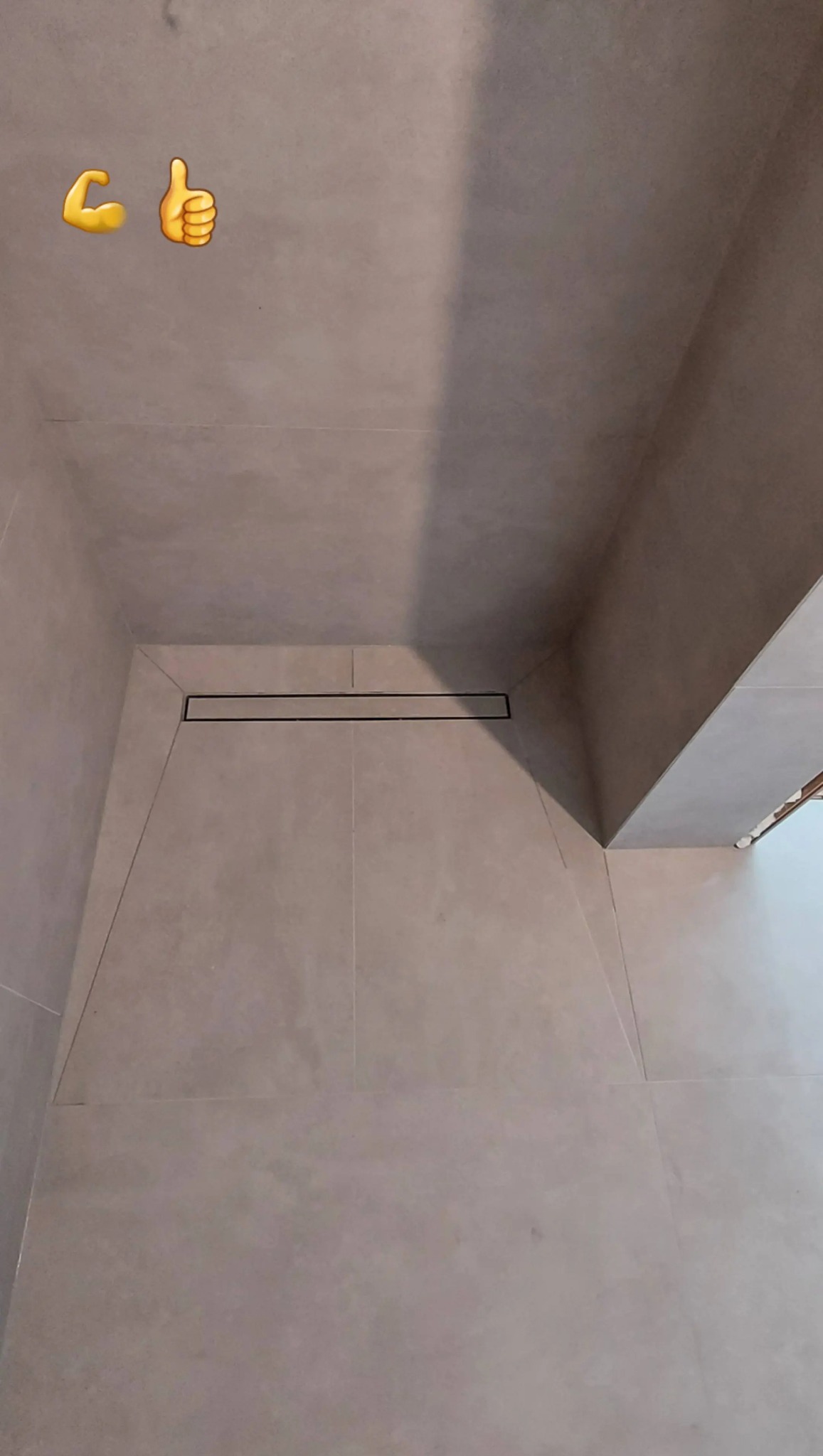 Wykończony brodzik z odpływem liniowym, wyłożony szarymi płytkami. W rogu widoczne emotikony 'siła' i 'kciuk w górę'.