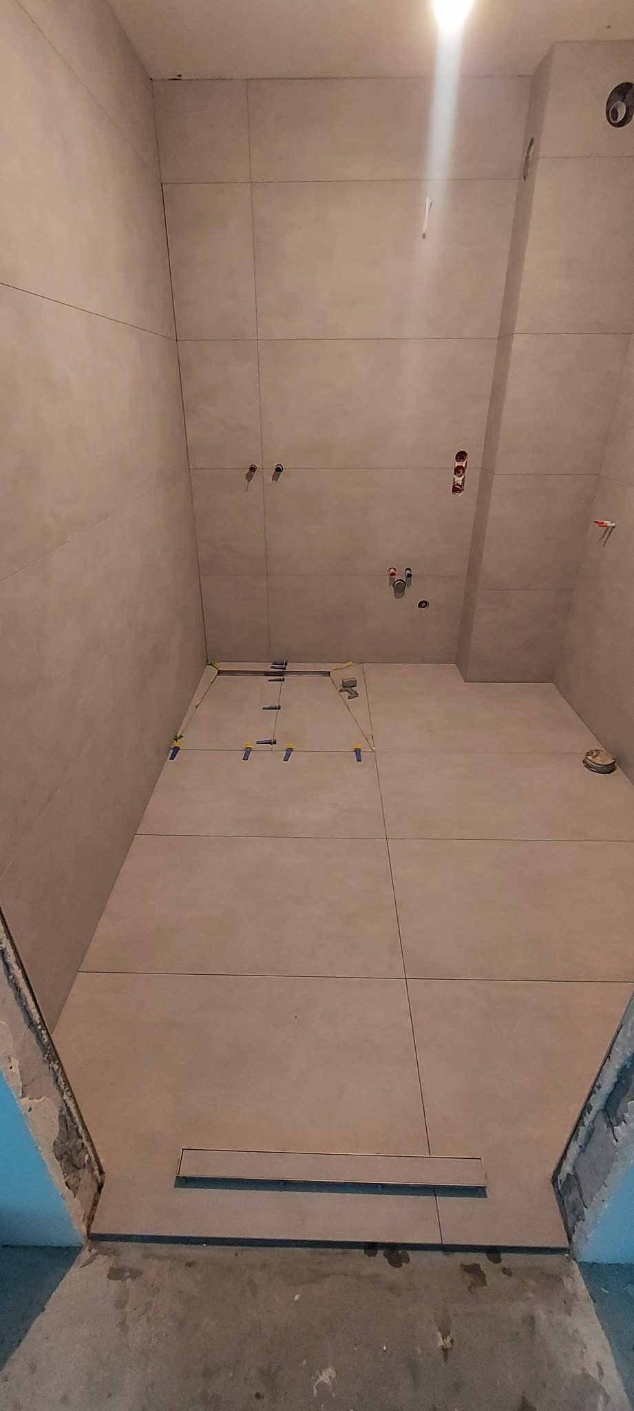 Wykończona, beżowa łazienka z odpływem liniowym w podłodze. Widoczne fugi i poziomowanie płytek. Otwory na armaturę.