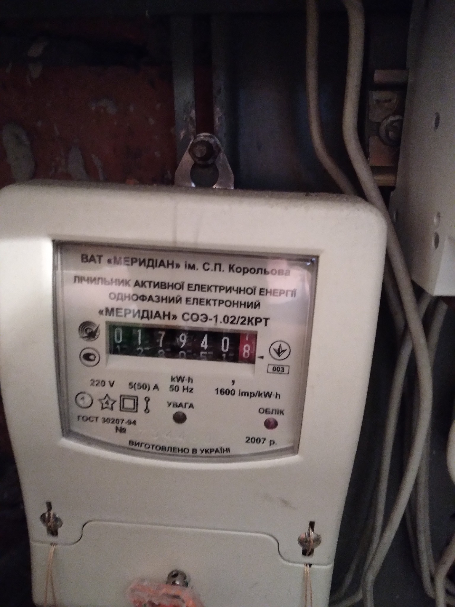 Licznik energii elektrycznej 'Meridian' z widocznym wskazaniem zużycia, zamontowany na ścianie z widocznymi przewodami. Wyprodukowano w Ukrainie w 2007 roku.