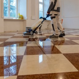 GRANITY SZCZEPAŃSKI - FILIP SZCZEPAŃSKI - Polerowanie szachownicy z kamienia. Pracownik używa maszyny polerskiej, odbicia okien w wypolerowanej podłodze. Granity Szczepański.