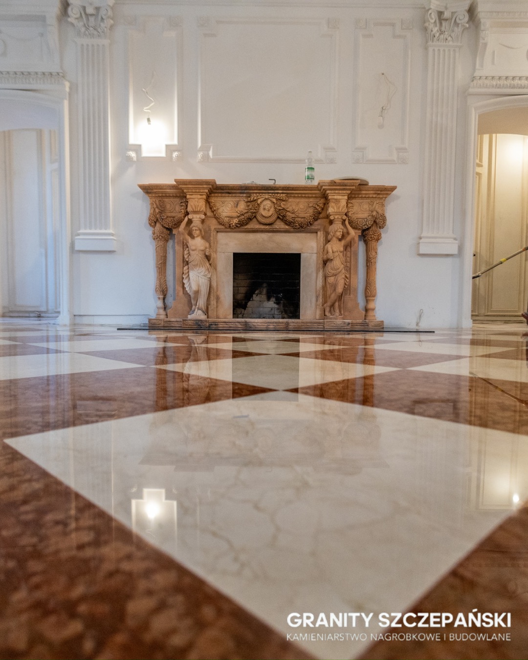 Elegancki kominek z rzeźbami i marmurowa podłoga w szachownicę, odbijająca światło. Klasyczne wnętrze z kolumnami i sztukaterią. Detal kamieniarski w luksusowym stylu.