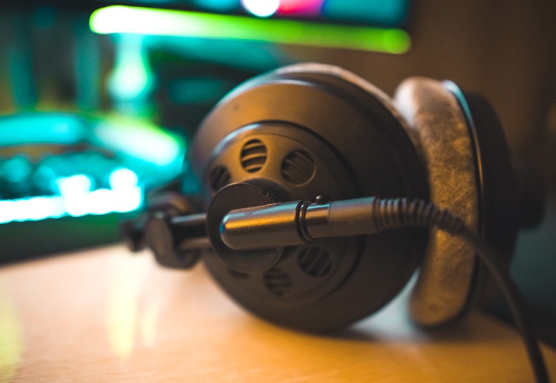 Profesjonalne słuchawki studyjne z podłączonym kablem, leżące na drewnianym blacie, z rozmytym ekranem komputera w tle. Sprzęt audio do monitoringu dźwięku.