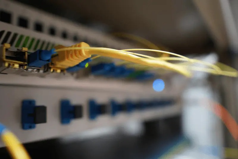 Żółty kabel światłowodowy podłączony do panelu krosowniczego z niebieskimi złączami. Widoczne diody LED sygnalizujące połączenie.