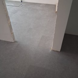 Volodymyr Shelest - Szara, matowa podłoga z paneli ułożona w nowym pomieszczeniu, widok z perspektywy wejścia, z fragmentem niedokończonego progu i widoczną instalacją elektryczną.