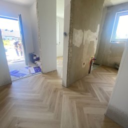 Volodymyr Shelest - Jasne panele ułożone w jodełkę w surowym wnętrzu. Widoczne ślady po pracach wykończeniowych na ścianach i otwarte przejście do kolejnego pomieszczenia.