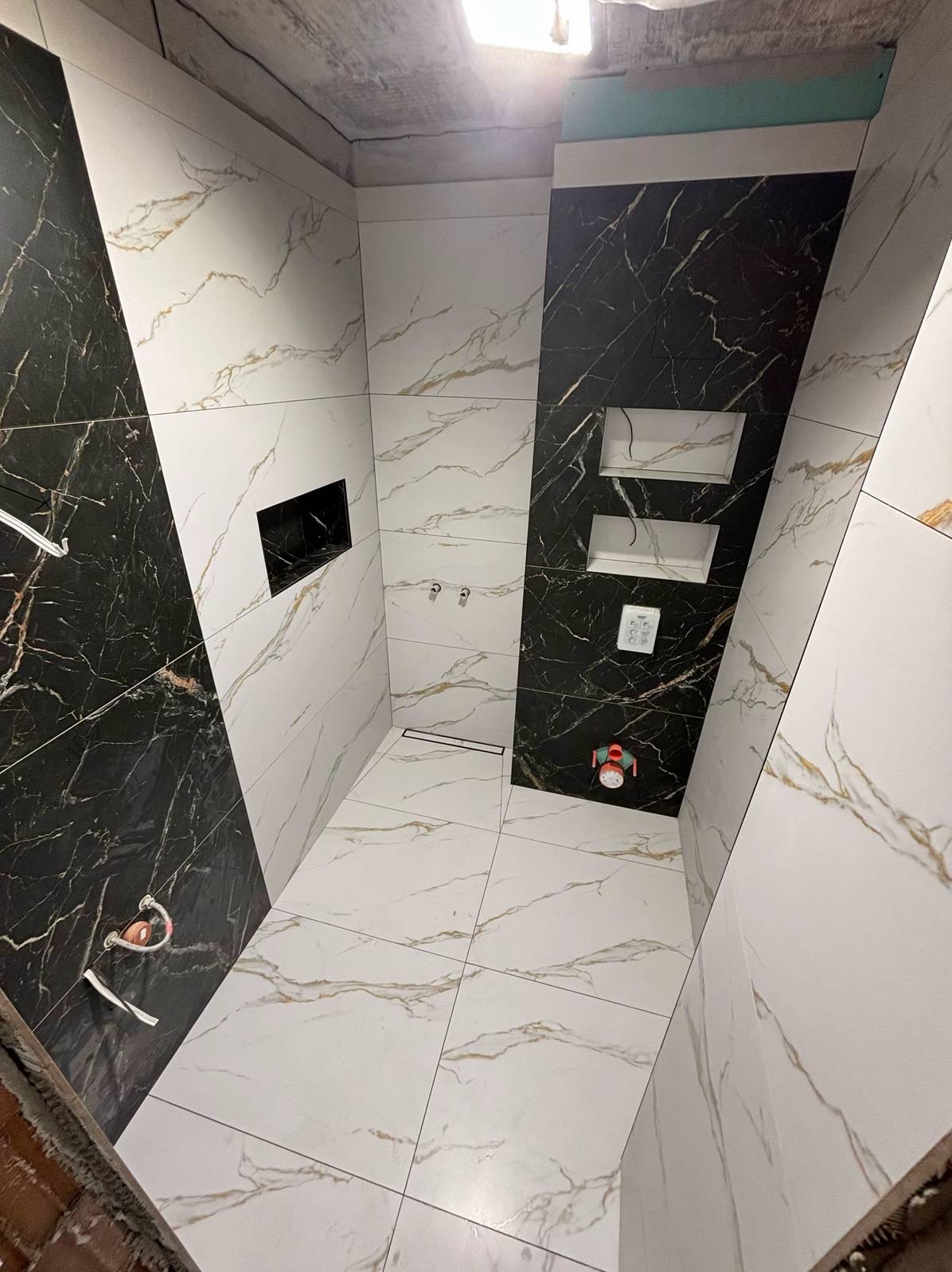 Elegancka łazienka w Warszawie z czarno-białymi płytkami imitującymi marmur. Widoczne wnęki w ścianie i odpływ liniowy w podłodze. Nowoczesny design.