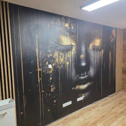 USŁUGI BUDOWLANE SOBKOWIAK DAWID - Wykończona łazienka z dekoracyjną fototapetą z motywem twarzy i drewnianymi lamelami na ścianie. Umywalka nablatowa z miedzianą armaturą. Parkiet na podłodze.