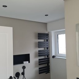 USŁUGI BUDOWLANE SOBKOWIAK DAWID - Minimalistyczna łazienka z wolnostojącą wanną, czarną armaturą i grzejnikiem drabinkowym. Oświetlenie punktowe w suficie. Neutralna kolorystyka ścian.