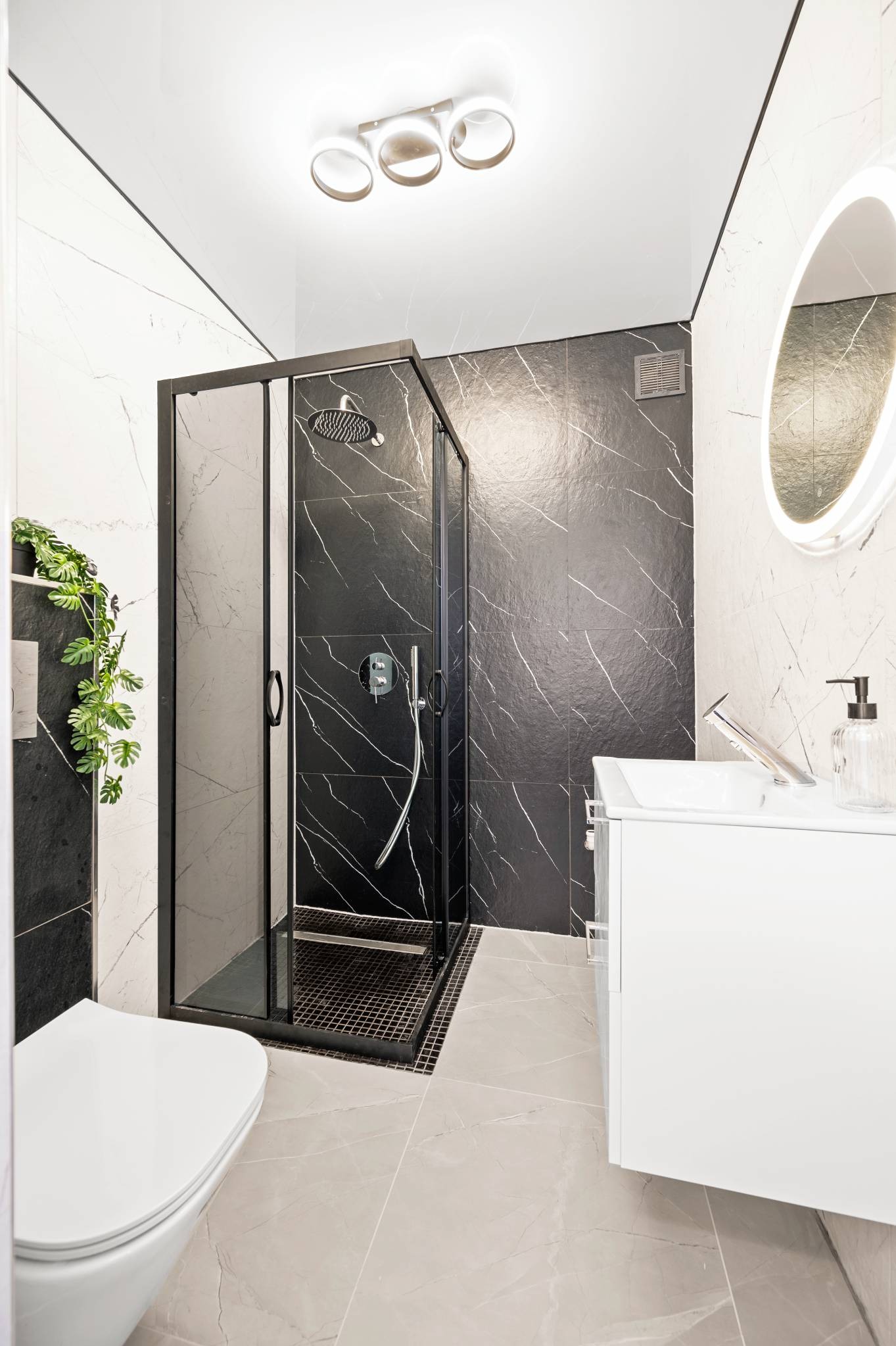 Nowoczesna łazienka z kabiną prysznicową typu walk-in, czarno-białymi marmurowymi płytkami i owalnym lustrem z podświetleniem LED. Minimalistyczny design.