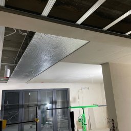 Damian Wójtowicz DW DreamWood - Sufit podwieszany z płyt karton-gips, częściowo z izolacją, widoczne profile i narzędzia montażowe. W tle okno balkonowe i instalacja elektryczna.