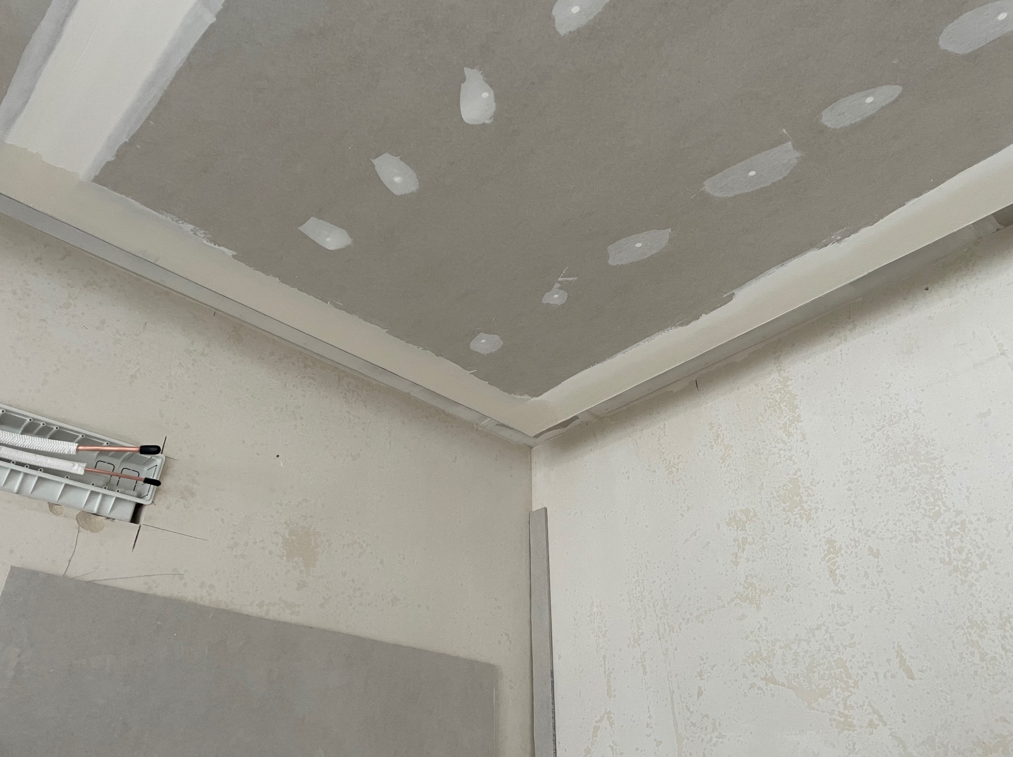 Sufit z płyt kartonowo-gipsowych w trakcie szpachlowania, widoczne łączenia i otwory po wkrętach. Fragment ściany z instalacją elektryczną w tle.