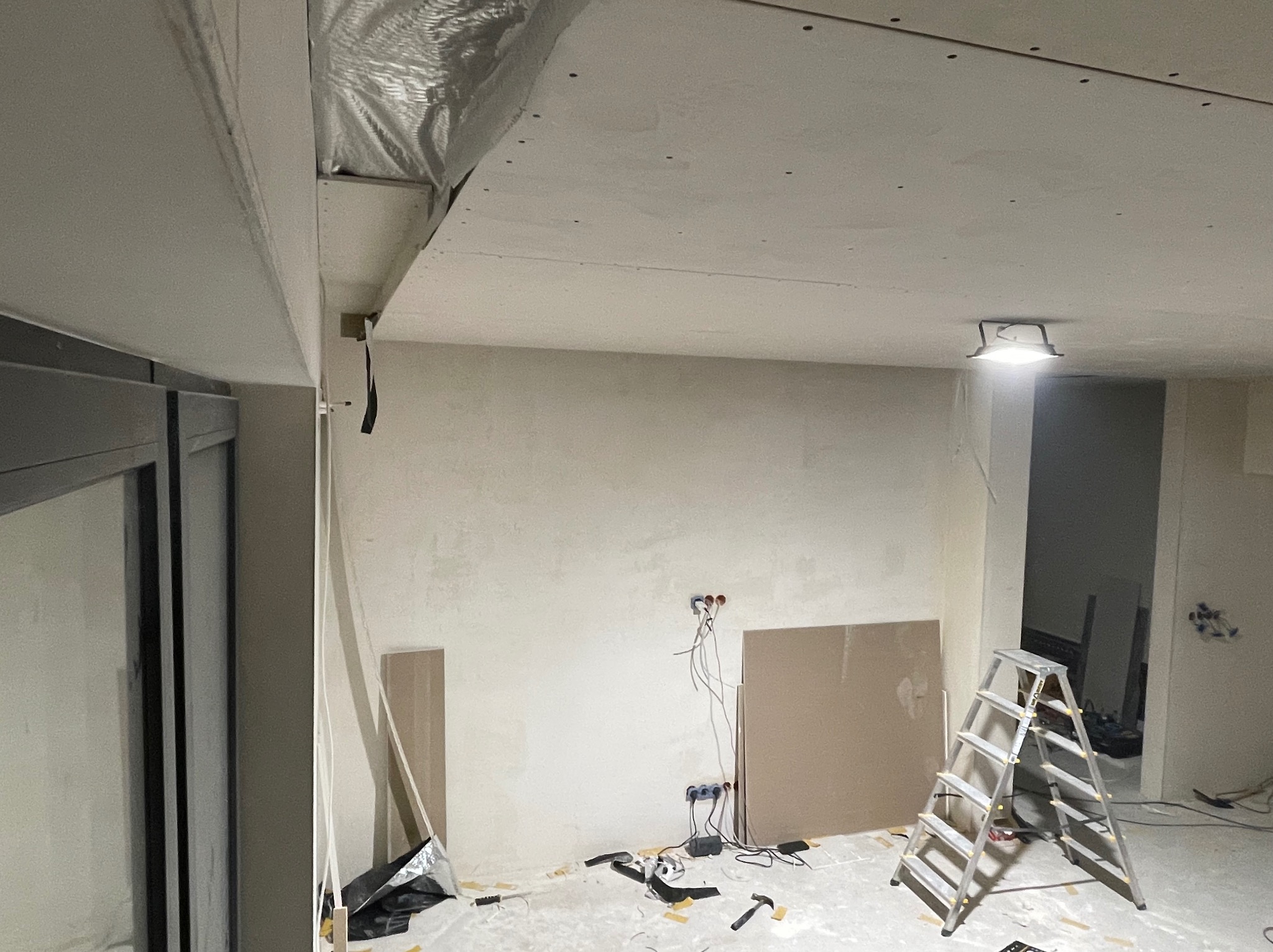 Wnętrze w trakcie remontu: widoczne płyty karton-gips na suficie i ścianach, instalacja elektryczna, drabina i narzędzia. Etap prac wykończeniowych w pomieszczeniu.