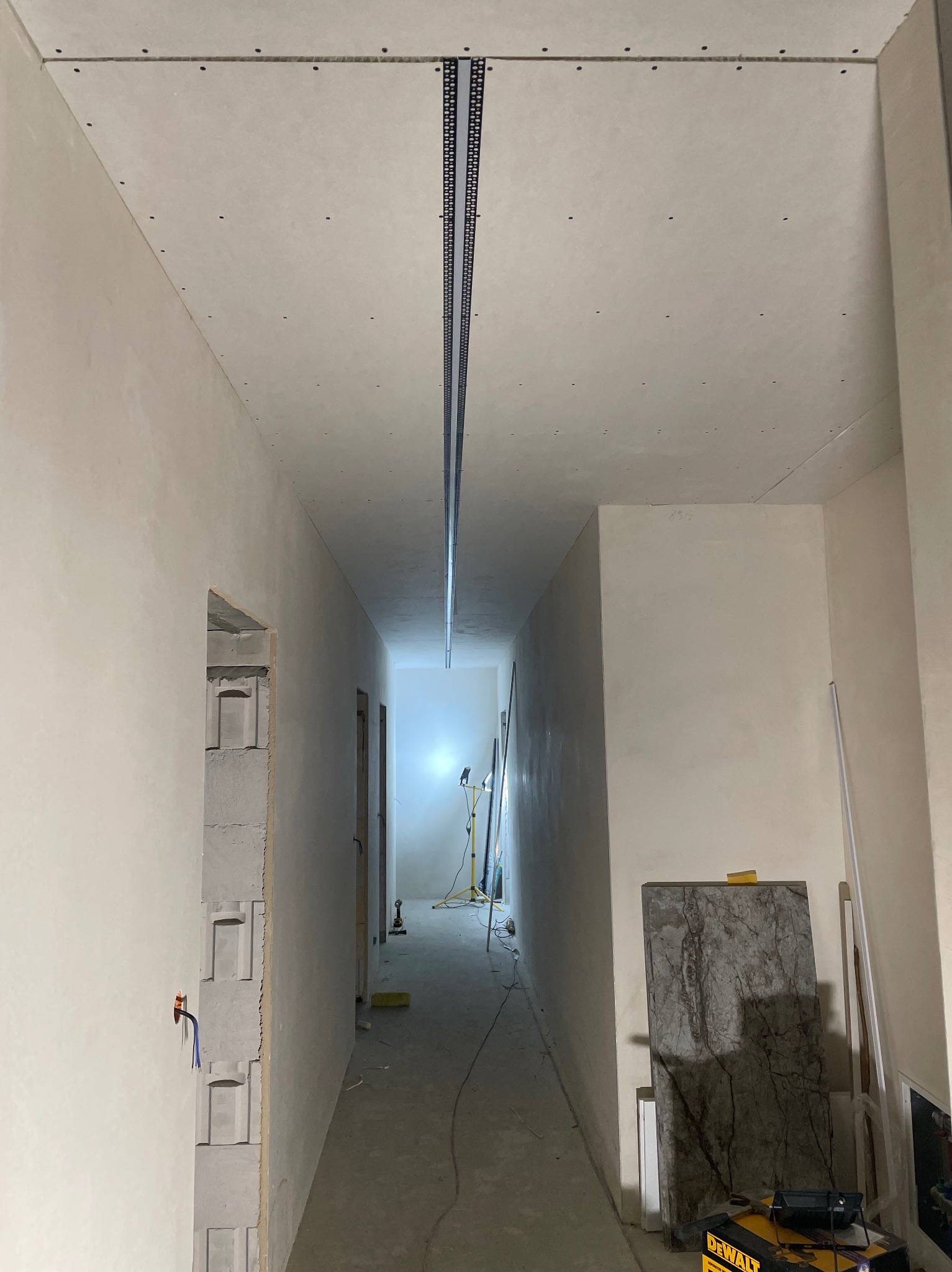 Korytarz w trakcie prac wykończeniowych: zamontowana listwa sufitowa, ściany przygotowane do malowania, widoczne narzędzia i materiały budowlane. Surowy stan.