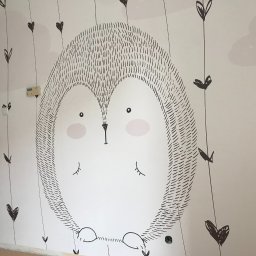 Krzysztof Dratwa - Ściana pokoju dziecięcego z ręcznie malowanym motywem jeża i serduszek. Minimalistyczny design, czarno-biała kolorystyka, widoczny fragment drzwi i podłogi.