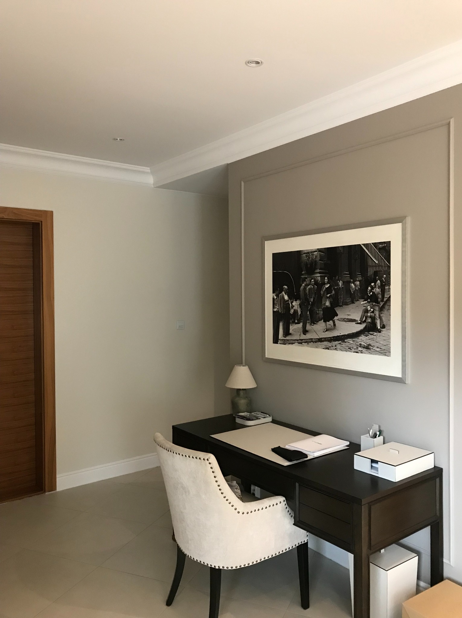 Pokój po malowaniu: beżowe ściany z białą sztukaterią, ciemne biurko z krzesłem w stylu glamour, na ścianie czarno-biała fotografia w ramie. Minimalistyczny design.